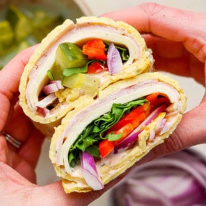 Hands holding a delicious cottage cheese wrap filled with turkey, lettuce, tomato, pickles, red onion, and spinach.