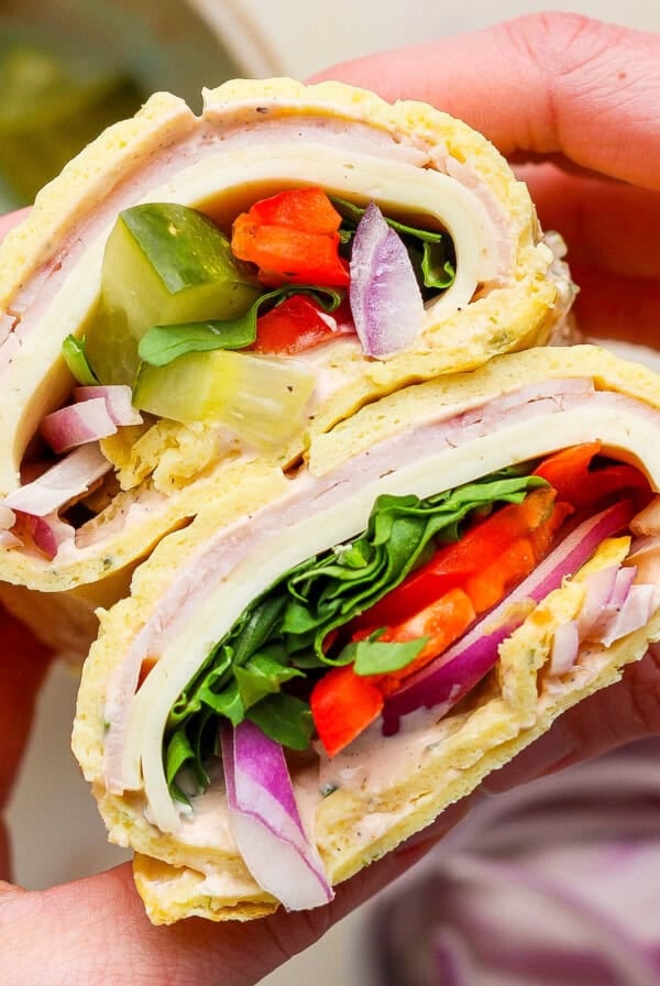 Hands holding a delicious cottage cheese wrap filled with turkey, lettuce, tomato, pickles, red onion, and spinach.