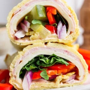 Close-up of a tortilla wrap cut in half, filled with turkey, cheese, lettuce, red onion, and bell peppers, on a white plate.