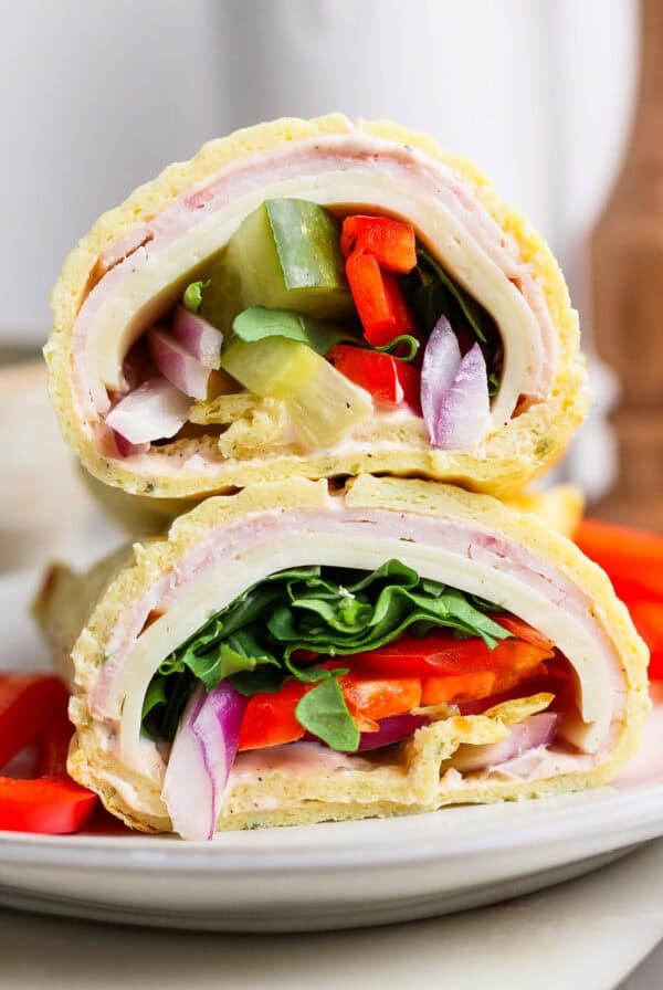 Close-up of two sandwich halves stacked, featuring layers of turkey, cheese, spinach, tomato, onion, and green pepper on a rolled flatbread. Resembling cottage cheese wraps in their wholesome appeal, they rest invitingly on a white plate.