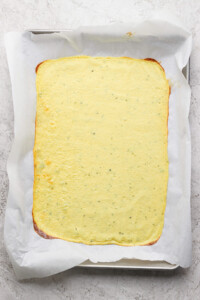 A rectangular sheet of pale yellow flatbread on parchment paper, placed on a baking tray.