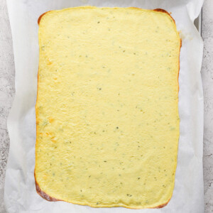 A rectangular sheet of pale yellow flatbread on parchment paper, placed on a baking tray.