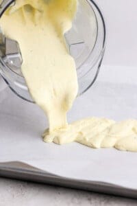 Thick yellow batter is being poured from a blender onto a lined baking sheet.