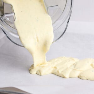 Thick yellow batter is being poured from a blender onto a lined baking sheet.