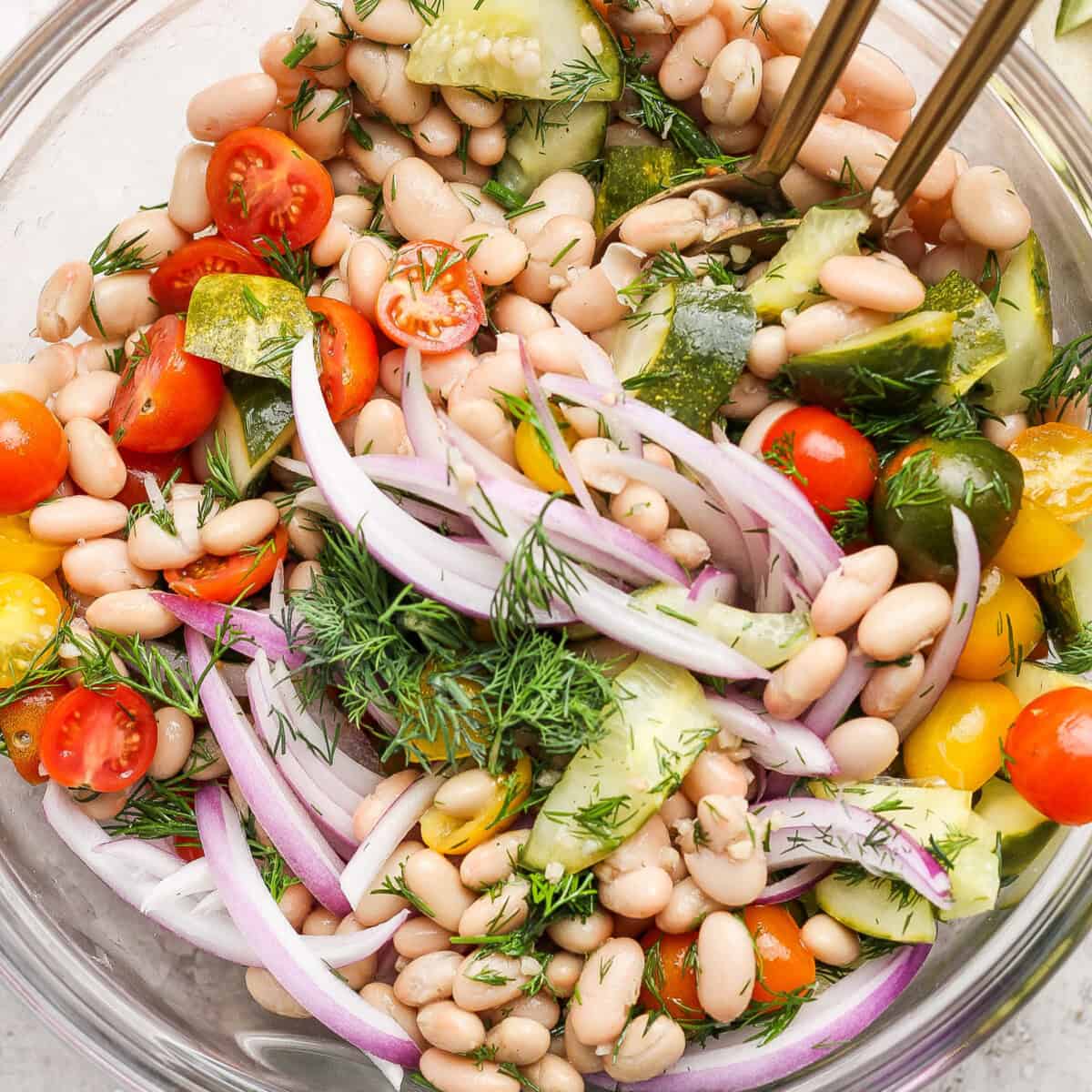 Bowl of white bean salad with cherry tomatoes, cucumber, red onion, and dill.