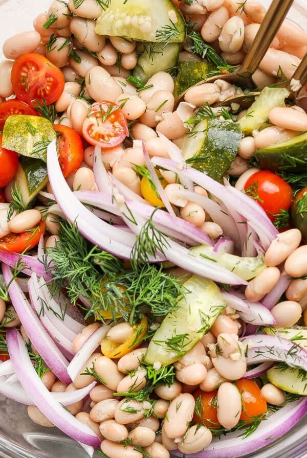 Bowl of white bean salad with cherry tomatoes, cucumber, red onion, and dill.