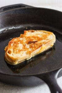 A grilled cheese sandwich sizzles in a black skillet, boasting a visible golden crust and slightly melted cheese, perfectly paired with a comforting bowl of tomato soup.