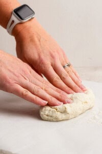 Hands with a watch and ring kneading dough on a white surface.