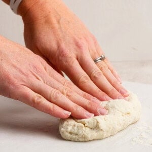 Hands with a watch and ring kneading dough on a white surface.