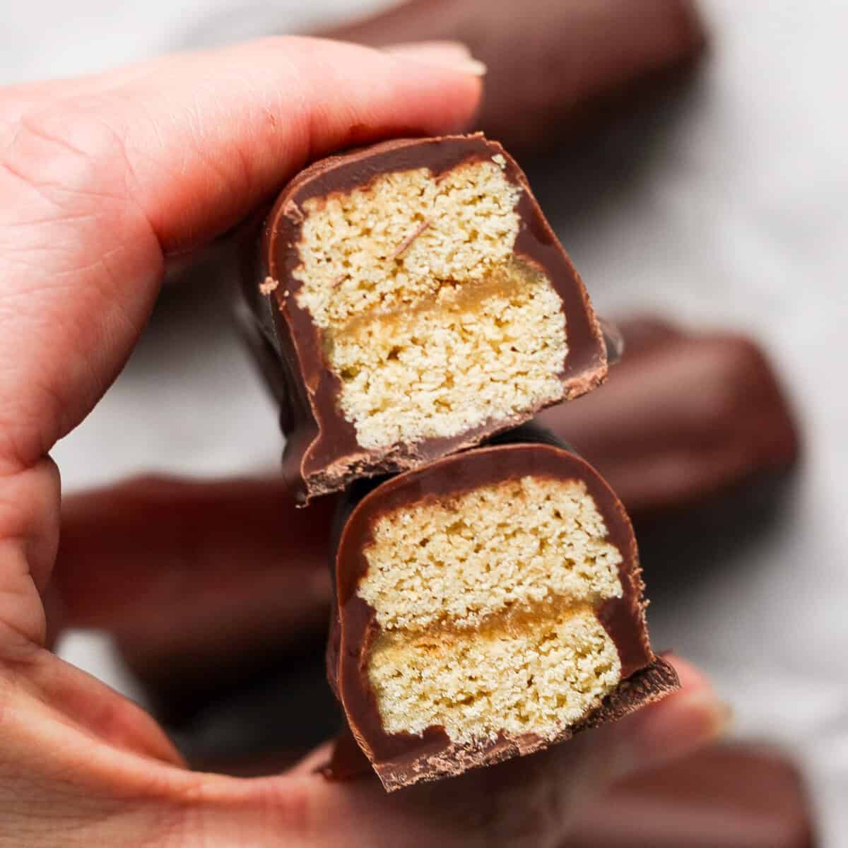 Close-up of a person holding a halved chocolate bar with layers of wafer and caramel filling visible inside.