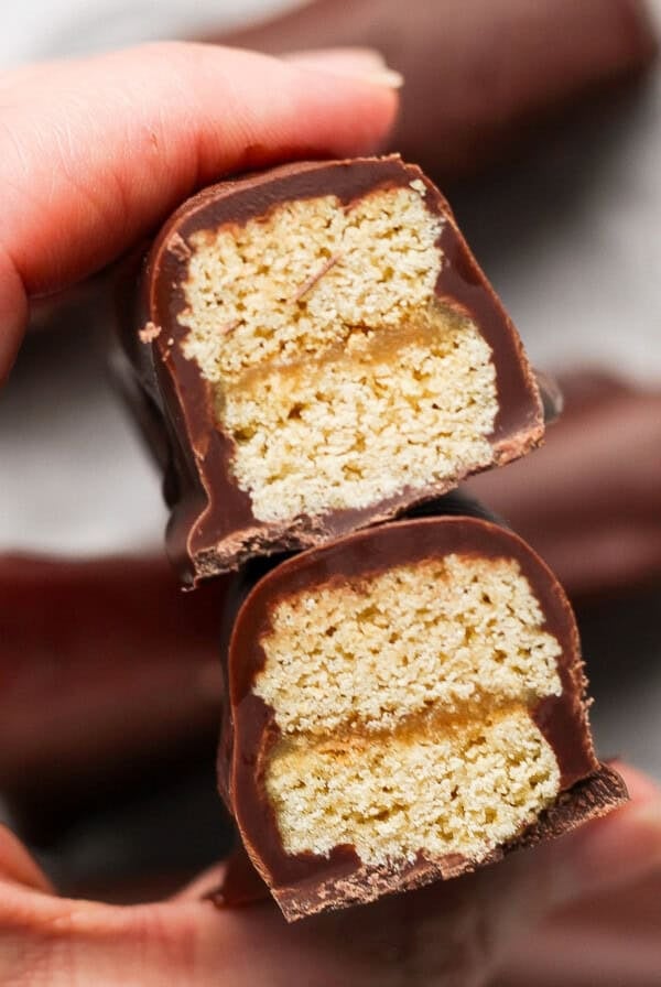 Close-up of a person holding a halved chocolate bar with layers of wafer and caramel filling visible inside.