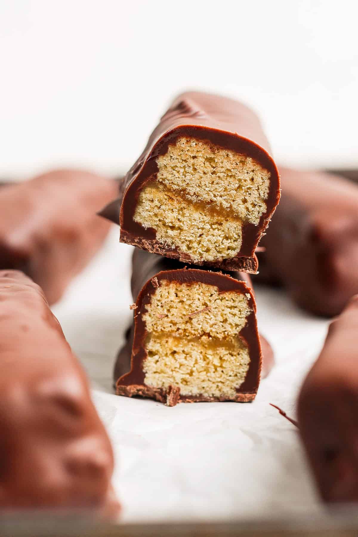 Two chocolate-coated biscuit bars stacked with one bisected, revealing a layered interior on a white surface.