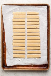 Strips of dough neatly arranged on a parchment-lined baking sheet.