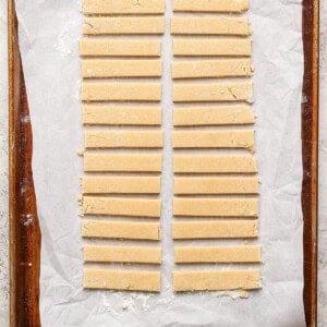 Strips of dough neatly arranged on a parchment-lined baking sheet.