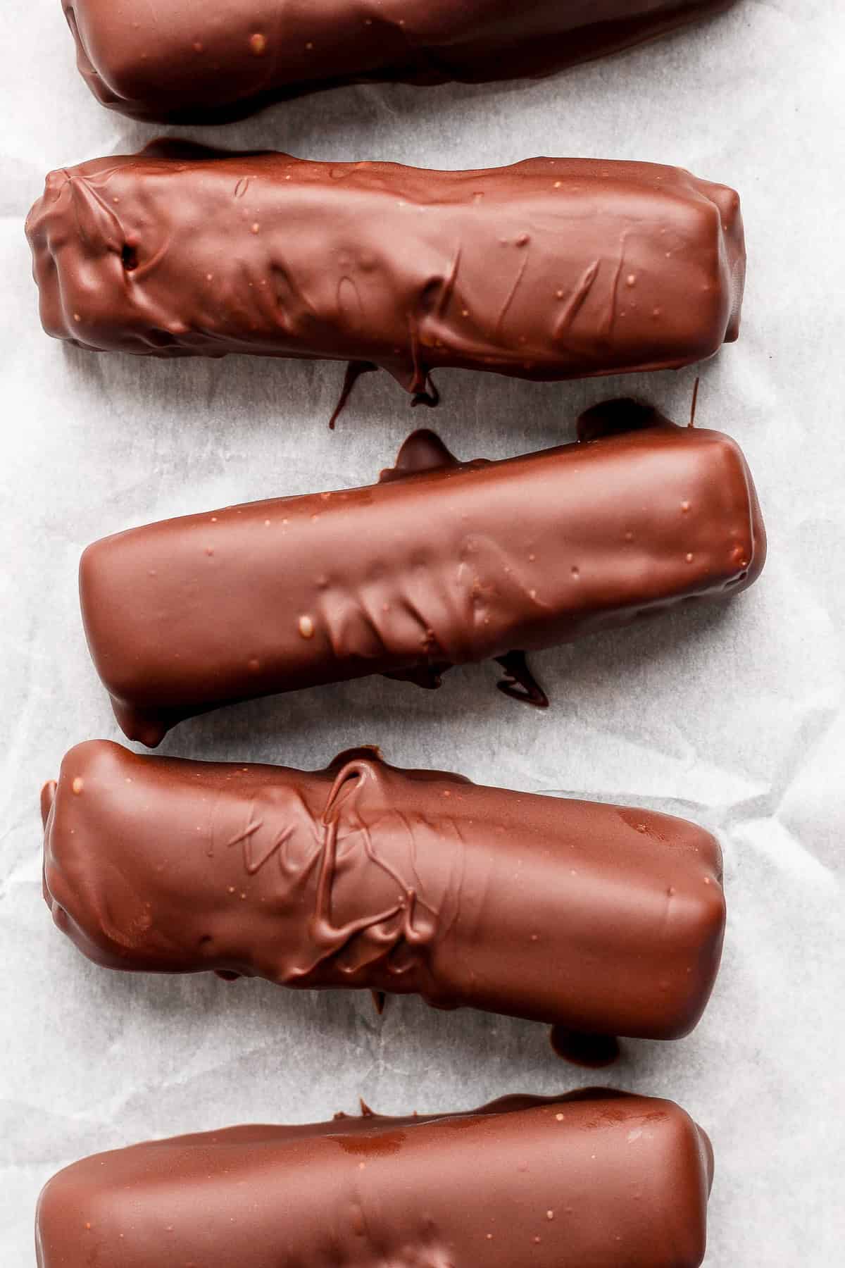 Five chocolate-coated bars arranged in a row on parchment paper.