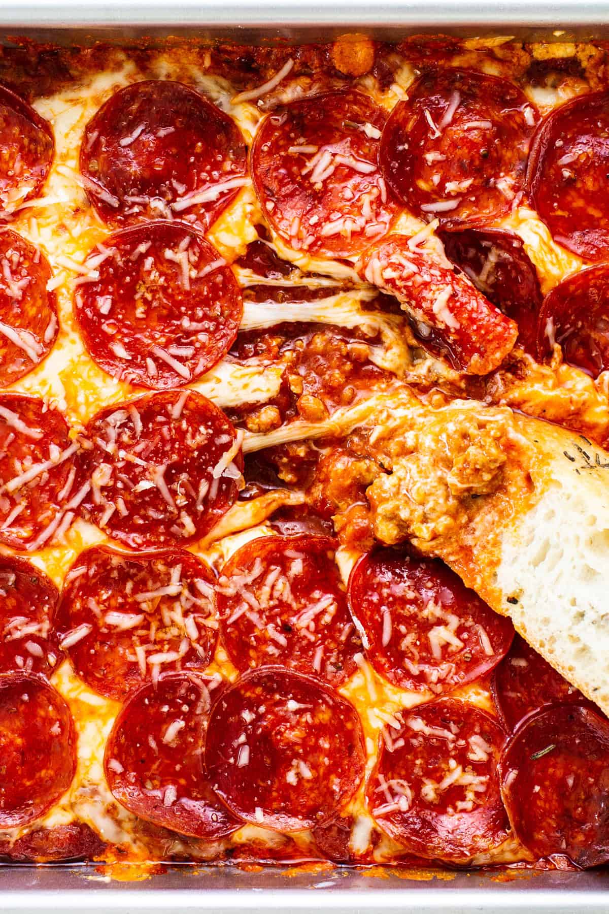 Close-up of a pepperoni pizza dip with melted cheese, pepperoni slices, and a piece of bread dipped into the mixture.