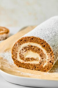A rolled cake dusted with powdered sugar on parchment paper, showing a spiral of cream filling.