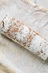 A rolled cake dusted with powdered sugar rests on a textured cloth.