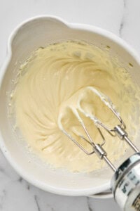 Electric mixer beaters in a bowl with creamy batter on a marble countertop.