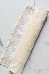 Rolled-up dough wrapped in a floured kitchen towel on a marble surface.