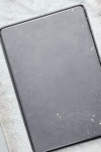 A rectangular, empty baking tray covered with a light dusting of flour on a textured surface.