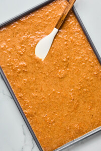 Baking tray filled with raw carrot cake batter and a spatula resting on top.