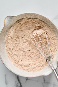 A bowl of dry ingredients is mixed with a metal whisk on a marble surface.