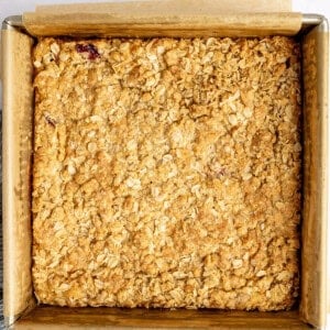 Square baking dish with a golden-brown baked oat crumble on parchment paper, resting on a light surface.