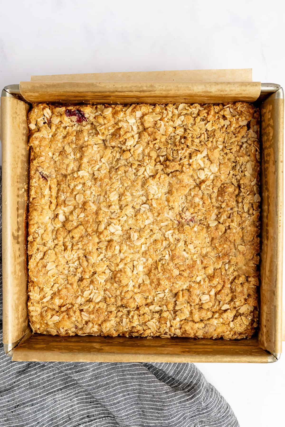 Square baking dish with a golden-brown baked oat crumble on parchment paper, resting on a light surface.