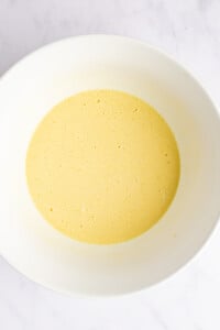 A bowl with yellow batter, slightly frothy, sits on a white surface.