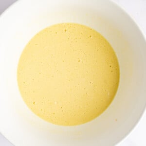 A bowl with yellow batter, slightly frothy, sits on a white surface.