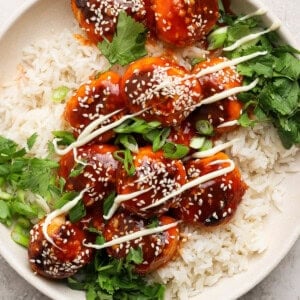 A plate of rice topped with glazed meatballs, sesame seeds, green onions, drizzled sauce, and fresh cilantro.