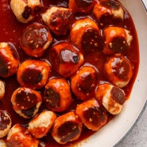 Meatballs in a skillet covered with a reddish-brown sauce.