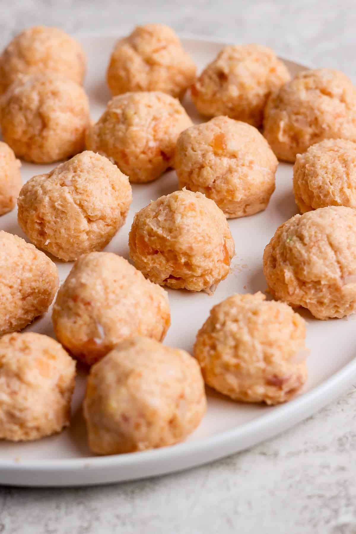 A plate of uncooked salmon balls arranged in rows on a white surface.