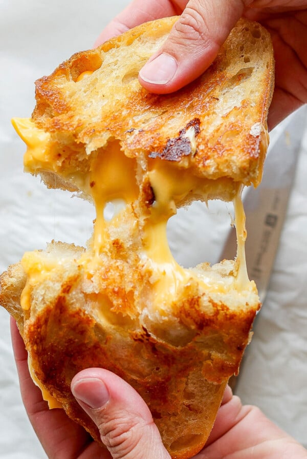 Hands pulling apart a grilled cheese sandwich, with melted cheese stretching between the toasted bread halves, creating a perfect pairing with creamy tomato soup.