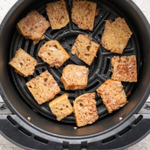 Pieces of bread being toasted in an air fryer basket.
