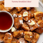 A plate of air fryer French toast bites topped with butter and served with syrup. Accompanied by strawberries and orange juice.