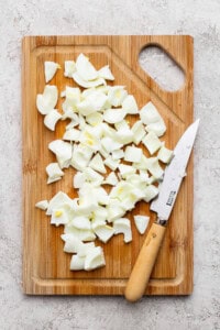 Chopped boiled eggs on a wooden cutting board with a knife on the side, placed on a light-colored surface.