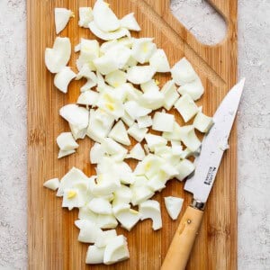 Chopped boiled eggs on a wooden cutting board with a knife on the side, placed on a light-colored surface.