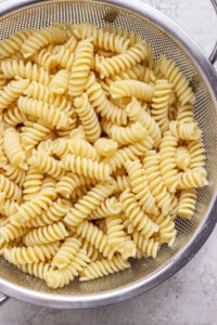 Cooked rotini pasta draining in a stainless steel colander.