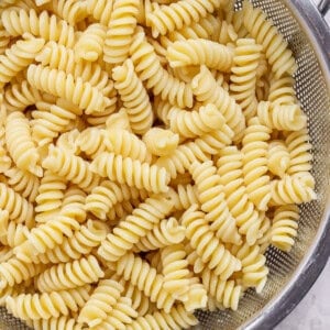 Cooked rotini pasta draining in a stainless steel colander.