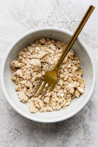 A bowl of dry oatmeal mixture with a gold fork placed inside on a textured surface.