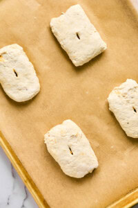 Four unbaked biscuit dough pieces, reminiscent of bubbling pizza crusts, rest on a parchment-lined baking sheet.