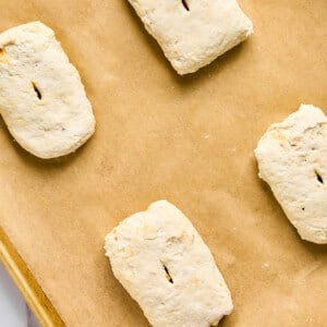 Four unbaked biscuit dough pieces, reminiscent of bubbling pizza crusts, rest on a parchment-lined baking sheet.