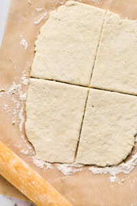 Rolled-out dough on parchment paper, cut into four sections like the perfect start for homemade pizza pockets, with a wooden rolling pin nearby.