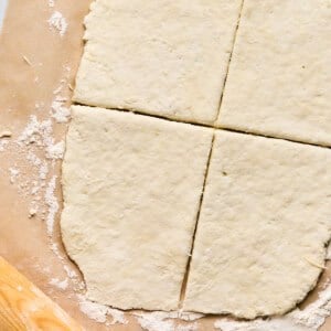 Rolled-out dough on parchment paper, cut into four sections like the perfect start for homemade pizza pockets, with a wooden rolling pin nearby.