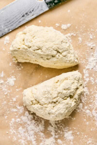Two pieces of dough sit on a floured surface next to a knife, ready to be transformed into homemade pizza pockets.