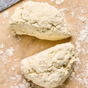 Two pieces of dough sit on a floured surface next to a knife, ready to be transformed into homemade pizza pockets.