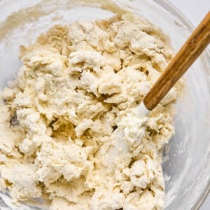 A glass bowl containing partially mixed dough with a wooden spoon sits ready to become delicious homemade pizza or hot pockets.