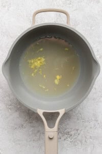 A gray saucepan filled with water and small yellow floral bits on a textured light gray surface.
